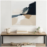 Abstract coastal landscape painting with layered beige sand tones, dark cliffs, and blue-gray sky, displayed above a wooden console holding a beige mug, books, and white vase.