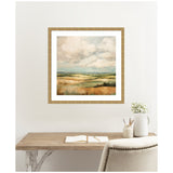 Framed abstract landscape painting of rolling hills under a cloudy sky, in soft greens, browns, and blues, hanging above a rustic wooden desk with open notebook and white vase.