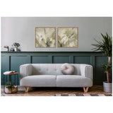 Two square abstract floral paintings in muted green and beige tones hang above a modern light gray sofa with angled wooden legs and a round textured pillow in a room with dark green wainscoting.