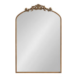 Arched rectangular mirror with slender gold frame topped by an ornate gold floral and scrollwork decoration centered at the arch peak.