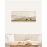 Framed horizontal landscape art print featuring soft beige and muted green hills with a textured brushstroke effect, hanging above a neutral beige sofa with a white pillow and wooden coffee table.
