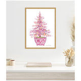 Framed watercolor painting of a pink Christmas tree decorated with colorful lights in a pink pot with floral patterns, displayed above a white shelf with neutral decor.