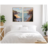 Two framed canvases above a white bed, each depicting coastal cliffs with pastel skies and ocean waves in soft, warm tones and impressionistic style.