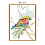 Watercolor painting of a small bird with vibrant yellow, pink, orange, and blue feathers perched on a leafy branch against a light blue background, framed in light wood.