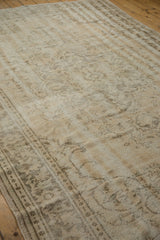 Faded vintage Oushak carpet with distressed ornate patterns in muted beige and gray tones on wooden floor.