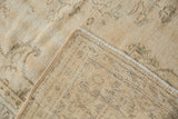 Close-up of a vintage distressed Oushak carpet in beige and light brown tones, showing intricate faded patterns and a slightly curled edge.
