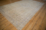 Large vintage Oushak carpet with a faded beige and light brown pattern laid on honey-colored hardwood floor, showing subtle geometric and floral wear.