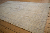Faded vintage Oushak carpet in pale beige and muted blue tones with distressed patterns, laid on honey-toned wooden floorboards.