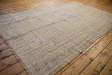 Large rectangular vintage Oushak carpet in muted beige and gray tones with subtle distressed patterns, laid on a honey-colored wooden floor.