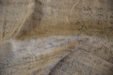 Close-up of a beige and brown vintage distressed Oushak carpet showing a textured weave with faint geometric and floral patterns.