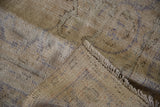 Close-up of a vintage distressed Oushak carpet in muted beige tones with faded blue and gray geometric patterns and fringed edges.