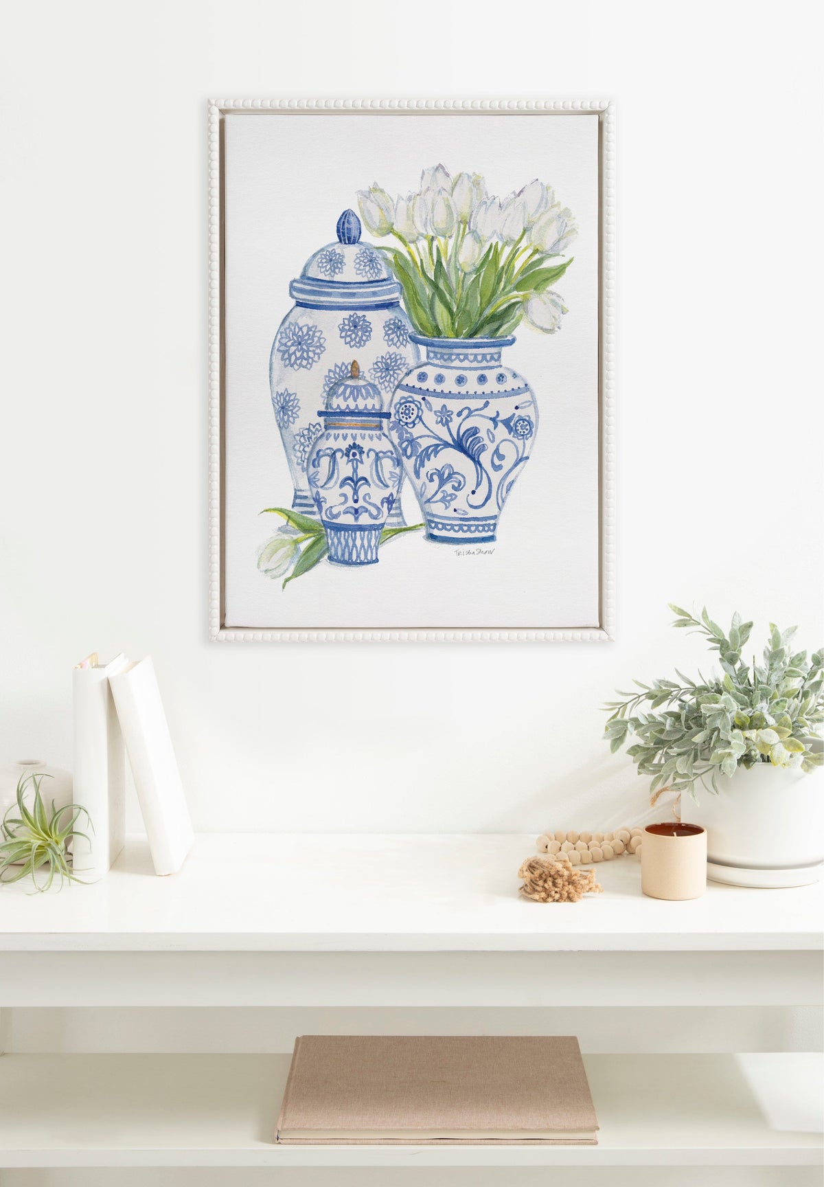 Framed canvas artwork by Patricia Shaw depicting three blue-and-white Chinoiserie jars with white tulips in the largest jar, displayed above a white mantel with decor.