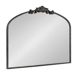 Rectangular wall mirror with a rounded arch top and ornate dark metal scrollwork decoration centered on the upper edge