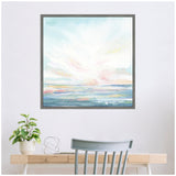 Framed canvas painting by Julie Maida depicting a pastel sky over a softly textured ocean, hung above a light wood desk with a green plant and decorative wire orb.