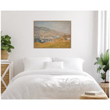 Framed landscape painting above white bed, depicting soft brown hills, distant blue water, and muted sky in warm earth tones, in a minimalist bedroom setting with plants.