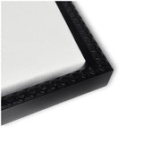 Close-up of a white canvas corner framed in glossy black with a raised bubble pattern along the inner edge of the frame