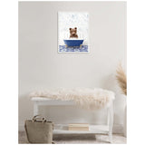 Framed canvas artwork of a brown bear cub sitting inside a small blue clawfoot bathtub, displayed on a light wall above a white bench with a fur throw and a beige bag on the floor.