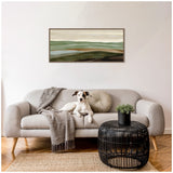 Minimalist living room with beige sofa featuring a gray throw and round cushion, a black round wicker coffee table with a small plant, and a framed abstract landscape artwork in green and beige tones hanging above.