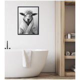 Black and white framed canvas of a sheep wearing a bathrobe, hanging above a white freestanding bathtub with a towel draped over the edge, next to wooden open shelving.