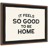 Black and white typography framed canvas art reading 'It Feels So Good to be Home' by Lucky Guava, set in a walnut brown Sylvie frame.