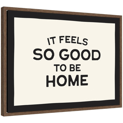 Black and white typography framed canvas art reading 'It Feels So Good to be Home' by Lucky Guava, set in a walnut brown Sylvie frame.