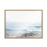 Framed print of a foggy seascape showing gentle waves approaching a rocky shore with soft blues and grays blending into a pale sky.