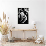 Black and white close-up photograph of flower petals in a silver frame mounted on a white wall above a wooden console table with wicker baskets and decorative dried plants beside it.