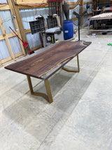 Handcrafted walnut slab table with clear resin finish and gold legs in a workshop setting
