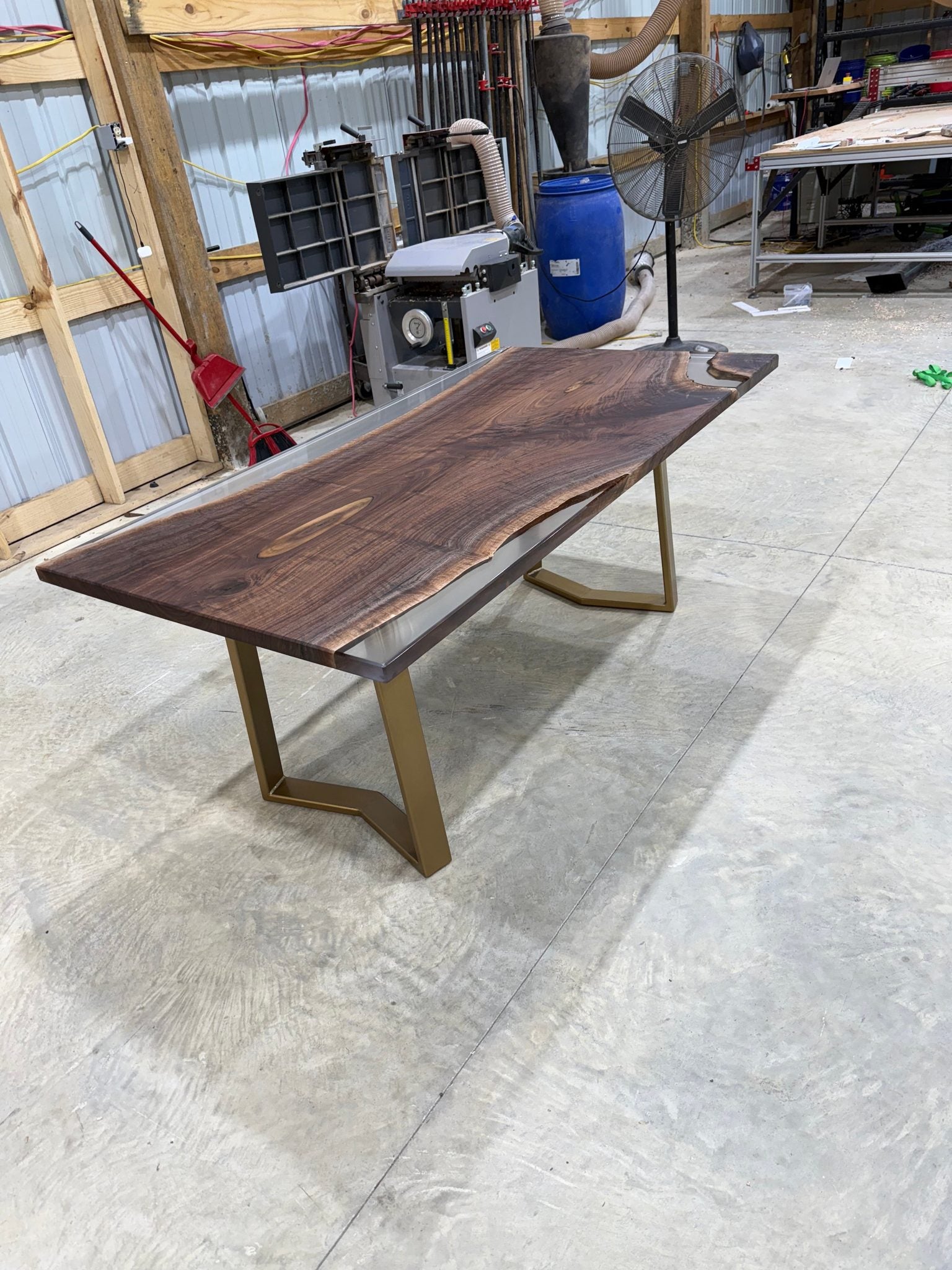 Handcrafted walnut slab table with clear resin finish and gold legs in a workshop setting