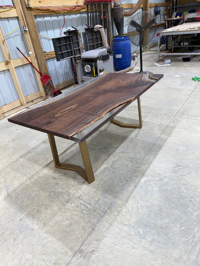 Handcrafted walnut slab table with clear resin finish and gold legs in a workshop setting