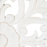 Close-up of white carved wood wall art featuring distressed finish with elegant swirling floral and shell-like patterns