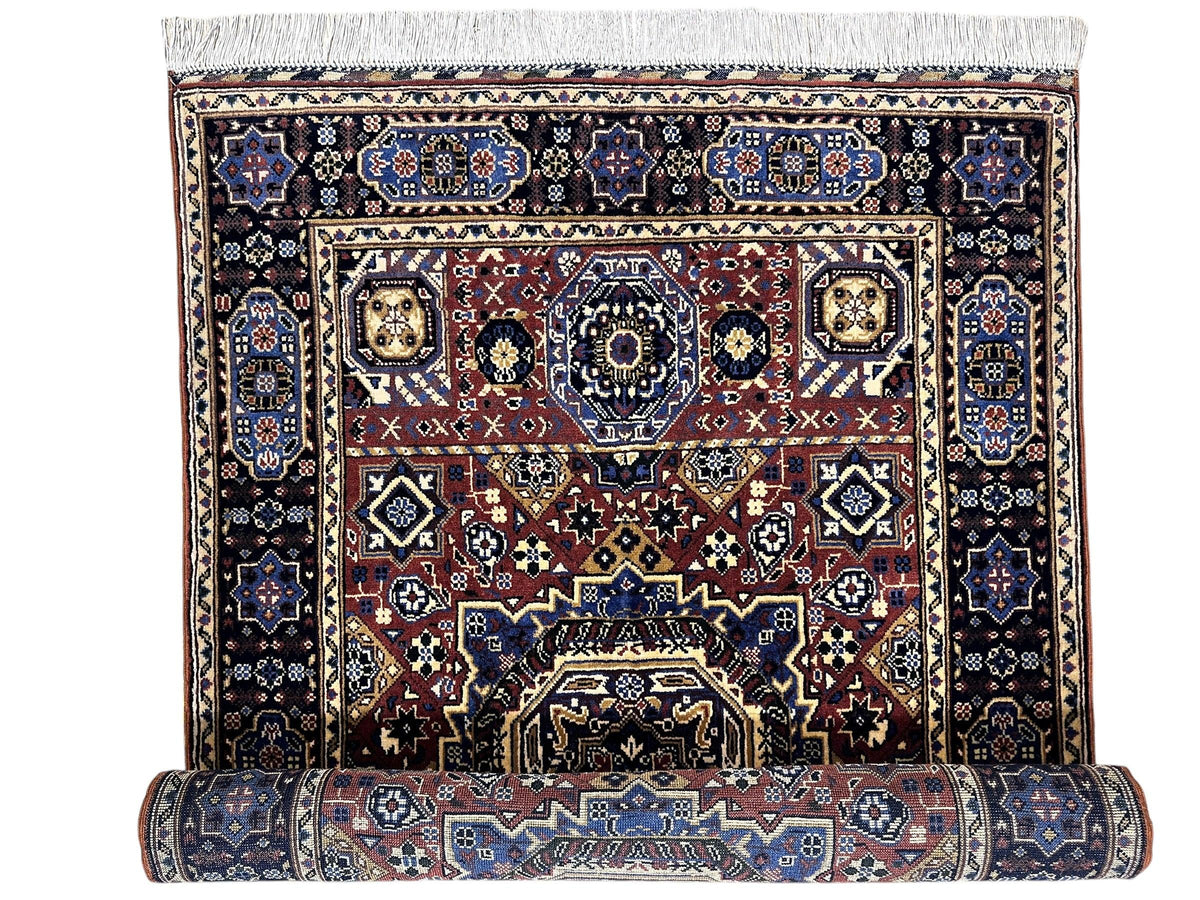 Hand-knotted Afghani Mamluk wool rug with intricate geometric patterns in blue, brown, and cream tones, partially rolled at the bottom showing detailed border design.