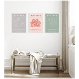 Three framed art prints on a white wall above a wooden bench with a white blanket; the prints feature minimalist white line drawings on pastel backgrounds labeled Picasso and Matisse.