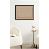 Rectangular beige pinboard with a black scallop border print, framed in black and mounted on a white wall between two white upholstered chairs and a small brass side table with a white vase.