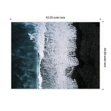Aerial view of deep blue ocean waves crashing onto a textured black sand beach with white foam creating a contrast between water and shore.