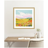 Square framed colorful meadow landscape painting with green and yellow fields, pink and white flowers under a blue sky with white clouds, hanging above a wooden desk.