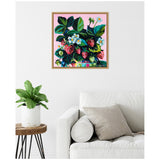 Framed canvas artwork of strawberries with green leaves and white flowers on a pink background, hanging above a white sofa and beside a potted plant on a wooden stool.