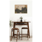 Dark wood tall table with two matching stools and a small black plant pot, beneath a framed landscape painting of a river and trees in muted earth tones.