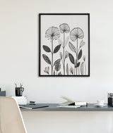 Black and white linocut print of stylized botanicals with large fan-shaped flowers and detailed leaves, framed and hung on a white wall above a tidy desk.