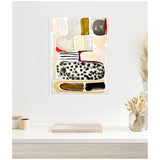 Abstract canvas with bold black and white spotted pattern, beige, yellow ochre, and red accents, framed and hanging above a white desk with neutral decor.