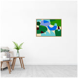 Abstract wall art with bold geometric shapes in blue, green, and beige tones, framed and hung above light wood floor and minimal furniture.