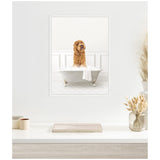 Framed canvas showing a curly brown Goldendoodle dog standing inside a white clawfoot bathtub against a light patterned wall, hung above a white modern desk with dried floral accents.