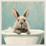 Gray and white fluffy bunny with large ears peeking over the edge of a white bathtub filled with water and bubbles against a soft blue background.