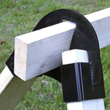 Close-up of a black metal quick stand clamp securing two white unfinished wood pieces against a grassy outdoor background.