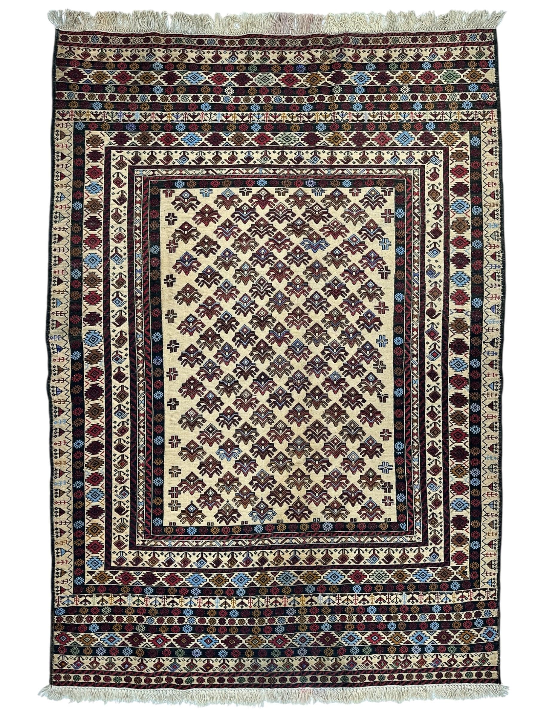 Hand-woven Afghani Maliki Soumak wool kilim rug laid on wood floor, displaying red and cream geometric patterns