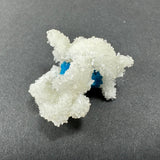 White crystalline stilbite with rough texture surrounding bright blue cavansite spheres on a dark gray background, showing intricate mineral formations.