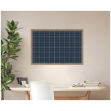 Rectangular navy blue fabric pinboard with a beige grid pattern and light wooden frame mounted on a beige wall above a light wood desk with chair and potted plant nearby