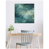 Abstract teal and green canvas with watery textures in a white frame, hanging above a light wood desk with a gray chair, small plant, and metal sculpture.