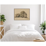 Sepia-toned framed canvas print of a pastoral landscape with large trees atop a small hill, hung above a white bed with layered pillows in a bright, minimal bedroom.