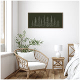 Minimalist sketch of evergreen trees in white on dark green background, framed and hung above a natural wood side table with white lamp in a bright room.